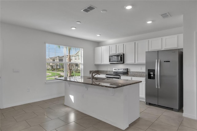 kitchen featuring an island with sink, appliances with stainless steel finishes, dark stone countertops, and white cabinets