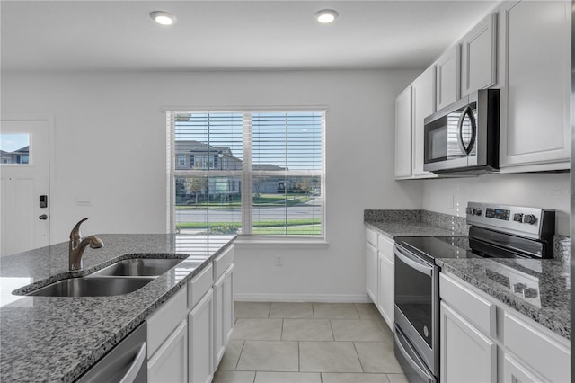 kitchen featuring sink, light tile patterned floors, appliances with stainless steel finishes, white cabinets, and stone countertops