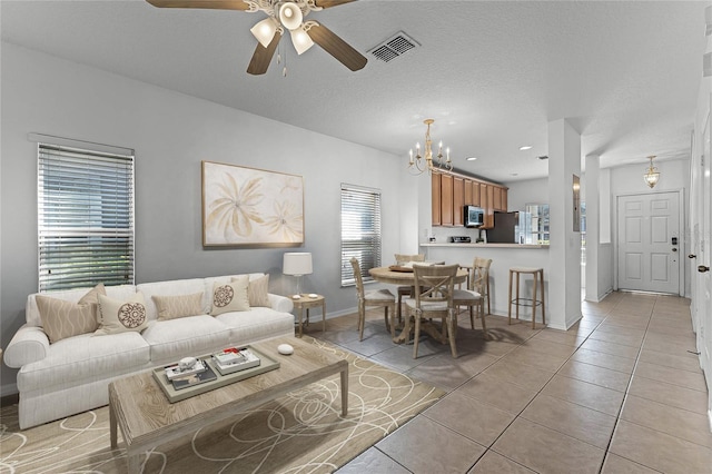 living room with visible vents, ceiling fan with notable chandelier, a textured ceiling, light tile patterned floors, and baseboards