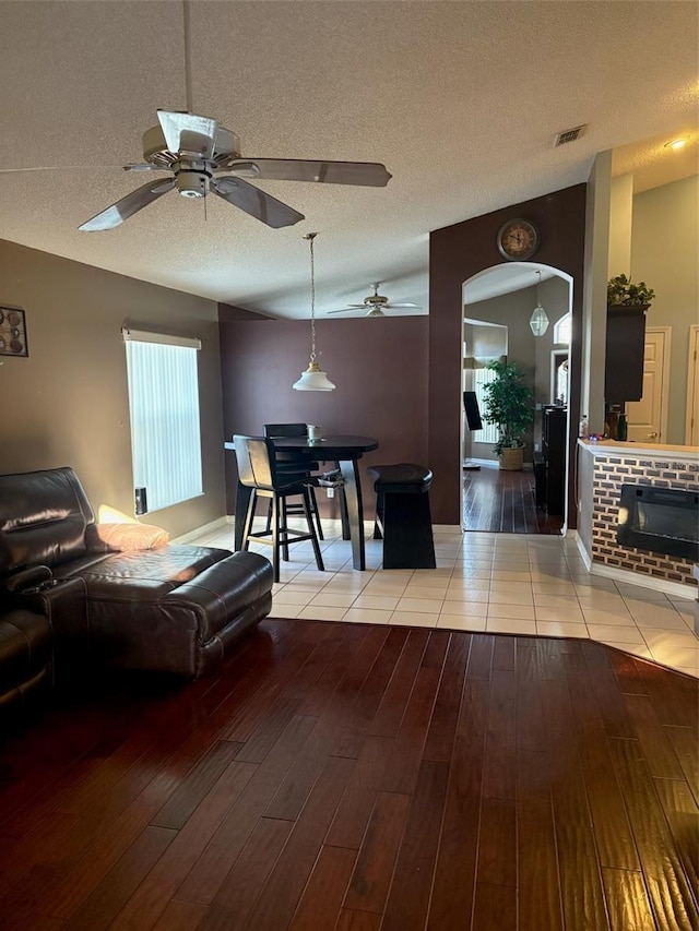 living room featuring ceiling fan, a fireplace, light hardwood / wood-style floors, and a textured ceiling