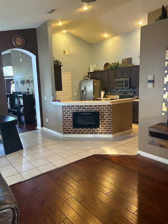 kitchen with stainless steel appliances, light tile patterned flooring, lofted ceiling, and dark brown cabinets