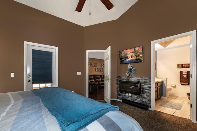 tiled bedroom featuring ceiling fan, a towering ceiling, a stone fireplace, and ensuite bath