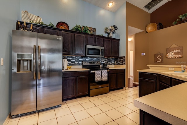 kitchen with appliances with stainless steel finishes, tasteful backsplash, dark brown cabinets, light tile patterned flooring, and sink