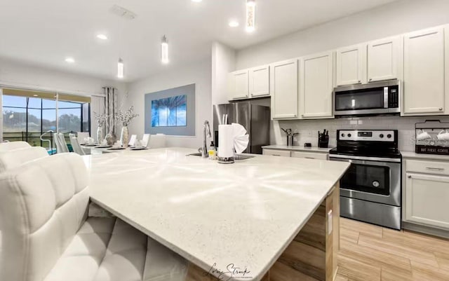 kitchen featuring stainless steel appliances, white cabinetry, and a kitchen island with sink