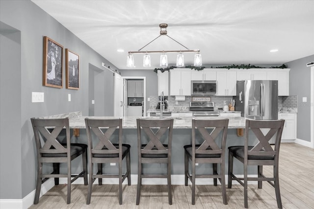 kitchen featuring appliances with stainless steel finishes, pendant lighting, white cabinets, a kitchen breakfast bar, and light stone countertops