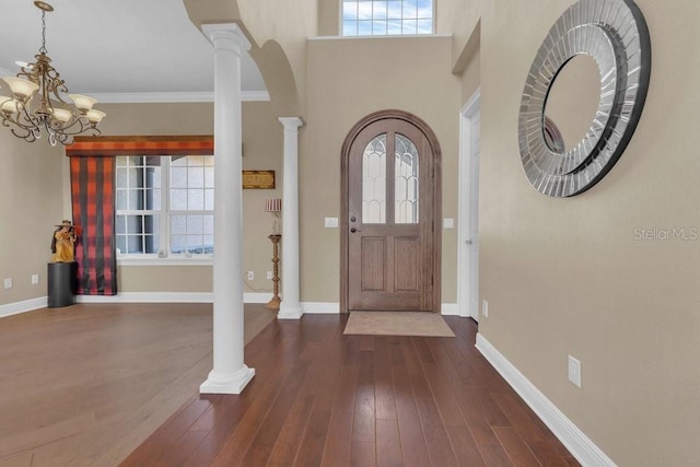 entryway with dark hardwood / wood-style flooring, crown molding, decorative columns, and a chandelier