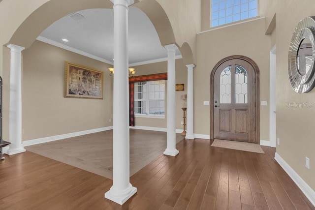 entrance foyer featuring ornate columns, wood-type flooring, a towering ceiling, and crown molding