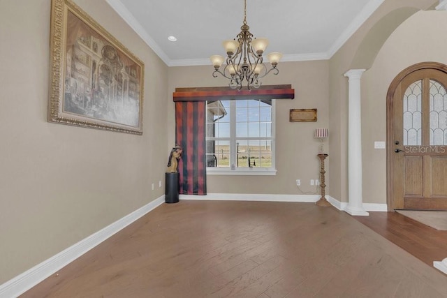 entrance foyer with crown molding, wood-type flooring, a chandelier, and ornate columns