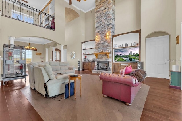 living room featuring a fireplace, hardwood / wood-style flooring, a high ceiling, crown molding, and an inviting chandelier