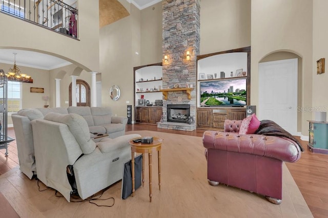 living room featuring an inviting chandelier, ornamental molding, hardwood / wood-style flooring, a fireplace, and decorative columns