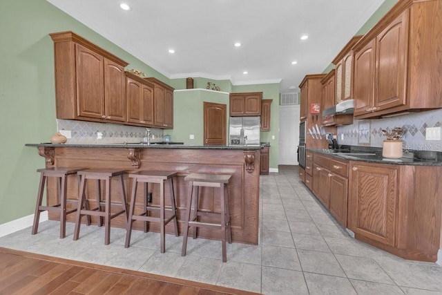 kitchen featuring crown molding, tasteful backsplash, stainless steel fridge, and a breakfast bar area