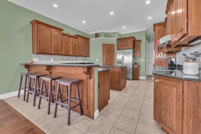 kitchen with a breakfast bar, crown molding, stainless steel fridge with ice dispenser, a kitchen island, and dark stone counters