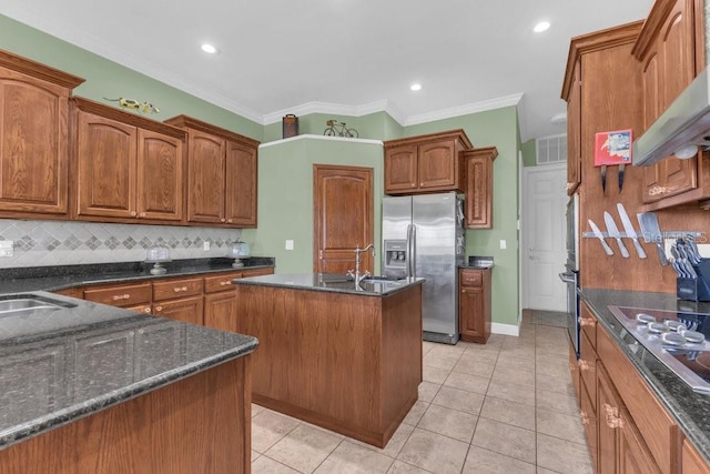 kitchen with appliances with stainless steel finishes, range hood, an island with sink, sink, and dark stone countertops