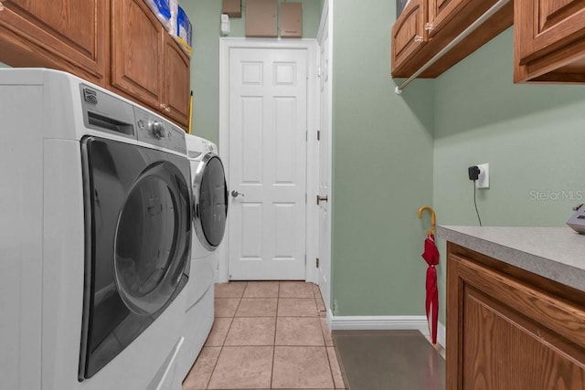 clothes washing area with washer and dryer, cabinets, and light tile patterned flooring