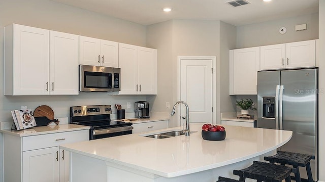 kitchen featuring sink, a breakfast bar area, appliances with stainless steel finishes, white cabinetry, and a center island with sink