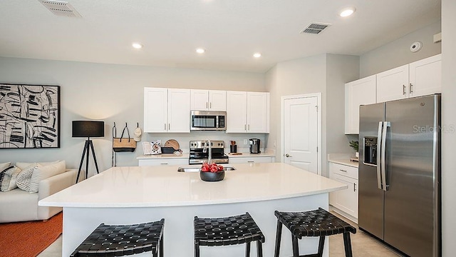 kitchen with sink, appliances with stainless steel finishes, a kitchen breakfast bar, an island with sink, and white cabinets