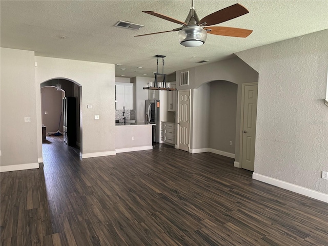 unfurnished living room with dark wood-type flooring, ceiling fan, sink, and a textured ceiling