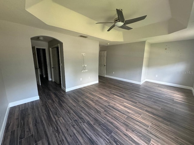 empty room with ceiling fan, dark hardwood / wood-style floors, and a raised ceiling