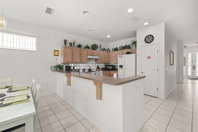 kitchen featuring sink, white appliances, a kitchen breakfast bar, light tile patterned flooring, and kitchen peninsula