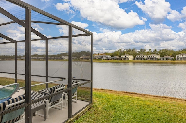 view of dock with a water view, a patio, glass enclosure, and a lawn