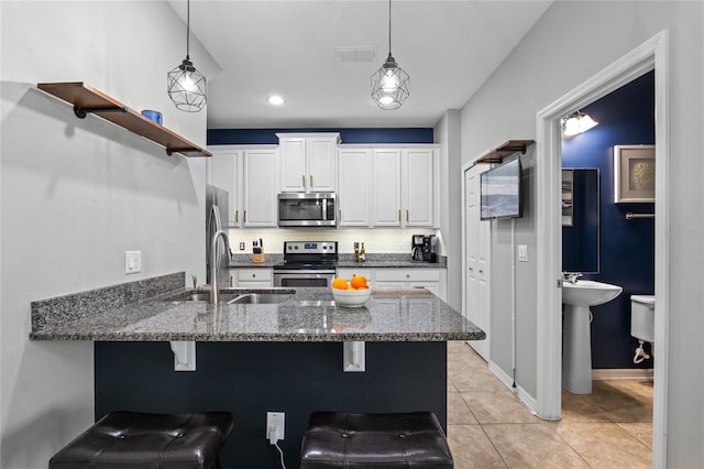 kitchen with a kitchen bar, sink, appliances with stainless steel finishes, pendant lighting, and white cabinets