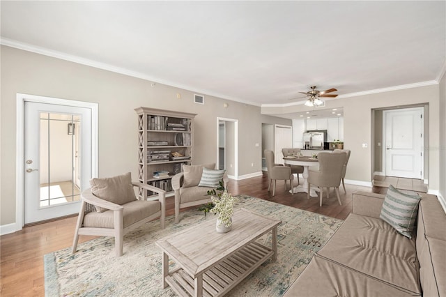 living area with ornamental molding, wood finished floors, visible vents, and baseboards