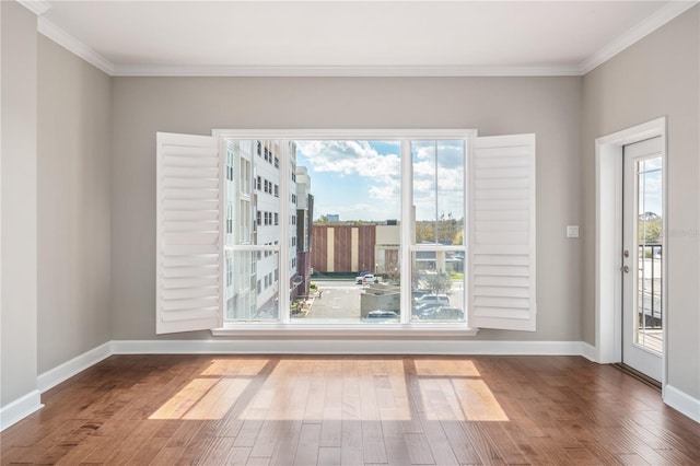 spare room featuring crown molding, baseboards, and wood finished floors