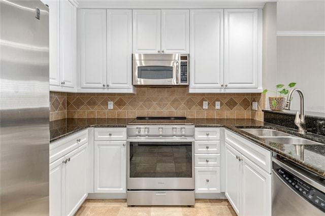 kitchen with appliances with stainless steel finishes, dark stone countertops, a sink, and white cabinets