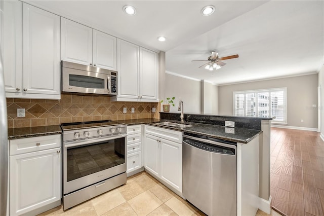 kitchen with dark stone countertops, a peninsula, stainless steel appliances, white cabinetry, and a sink