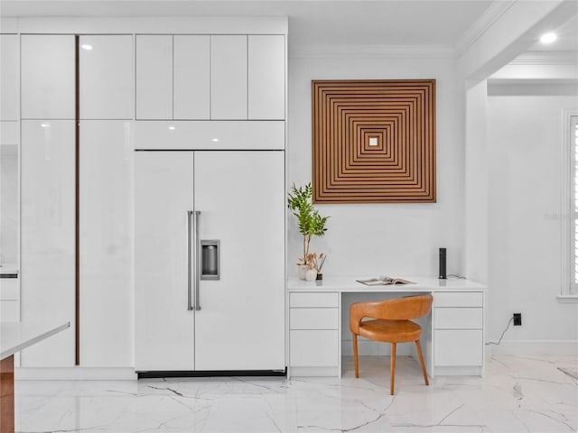 kitchen featuring ornamental molding, paneled refrigerator, built in desk, and white cabinets