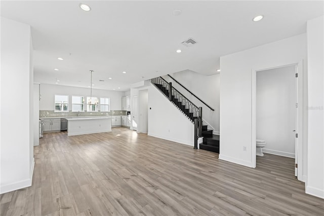 unfurnished living room with an inviting chandelier and light hardwood / wood-style flooring