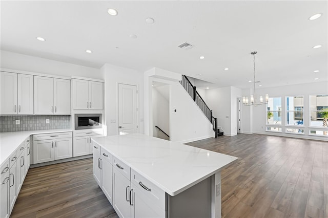 kitchen with stainless steel microwave, tasteful backsplash, white cabinetry, a center island, and light stone countertops