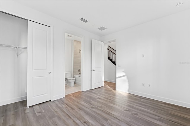 unfurnished bedroom featuring ensuite bath, light wood-type flooring, and a closet