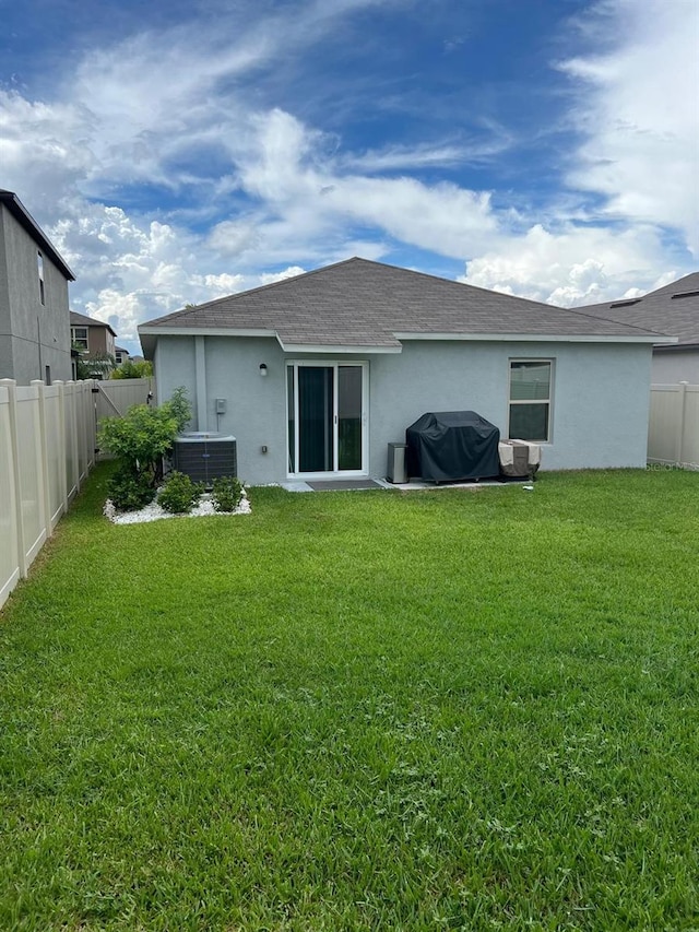 rear view of house featuring central AC and a lawn