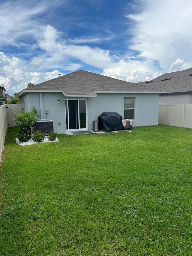 rear view of property with central AC and a yard