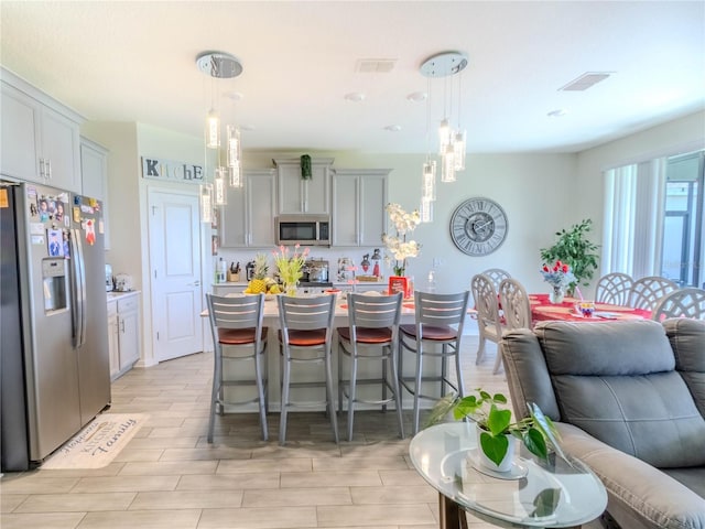 kitchen with a center island, hanging light fixtures, appliances with stainless steel finishes, a kitchen breakfast bar, and gray cabinets