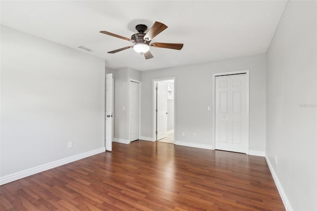 unfurnished bedroom featuring two closets, dark hardwood / wood-style floors, and ceiling fan