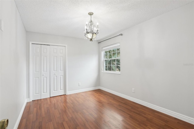 unfurnished bedroom featuring hardwood / wood-style flooring, a chandelier, a closet, and a textured ceiling