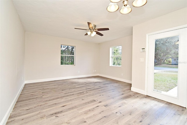 spare room with ceiling fan with notable chandelier and light wood-type flooring