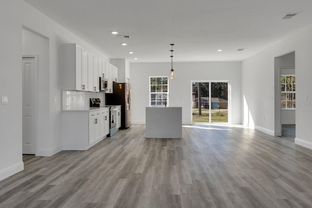 kitchen featuring light wood-type flooring, white cabinets, pendant lighting, stainless steel appliances, and backsplash