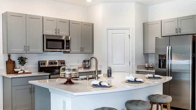 kitchen with gray cabinetry, a center island with sink, a breakfast bar, and appliances with stainless steel finishes