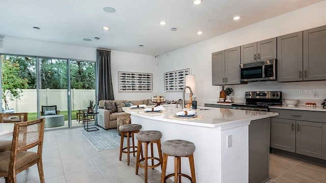 kitchen featuring gray cabinetry, sink, a center island with sink, and appliances with stainless steel finishes