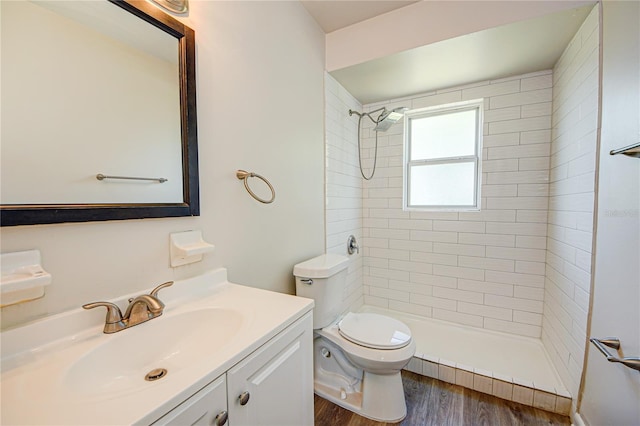 bathroom featuring hardwood / wood-style flooring, vanity, a tile shower, and toilet