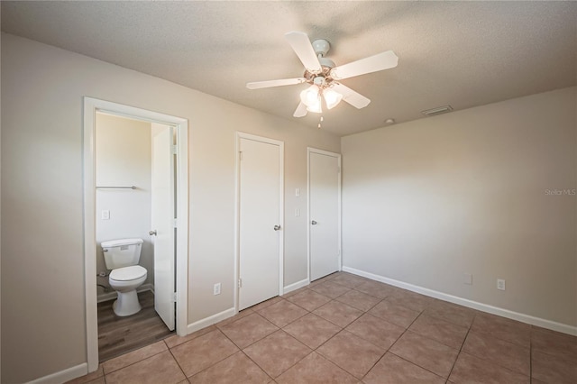 unfurnished bedroom with ceiling fan, light tile patterned floors, a textured ceiling, and ensuite bath