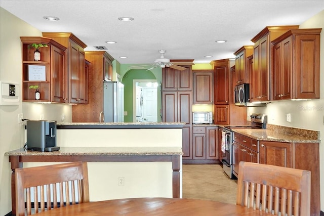 kitchen with light stone counters, ceiling fan, stainless steel appliances, and kitchen peninsula