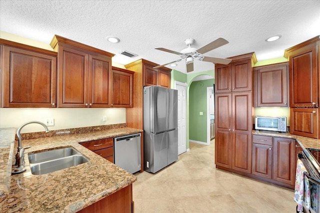 kitchen with sink, a textured ceiling, ceiling fan, stainless steel appliances, and light stone countertops