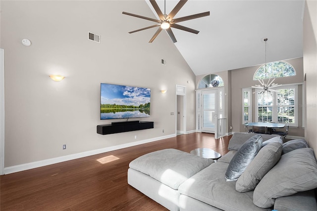 living room featuring dark wood-type flooring, ceiling fan with notable chandelier, and high vaulted ceiling