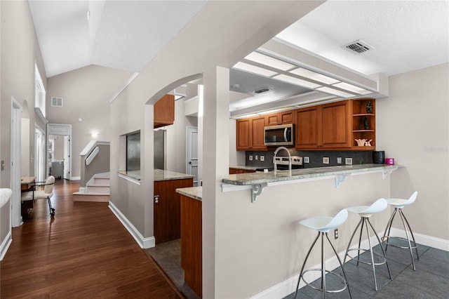 kitchen with light stone countertops, stainless steel appliances, kitchen peninsula, and a kitchen bar