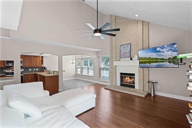 living room featuring sink, wood-type flooring, high vaulted ceiling, a brick fireplace, and ceiling fan