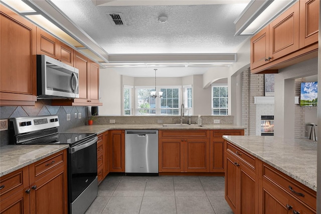 kitchen featuring appliances with stainless steel finishes, a fireplace, decorative light fixtures, sink, and light stone countertops